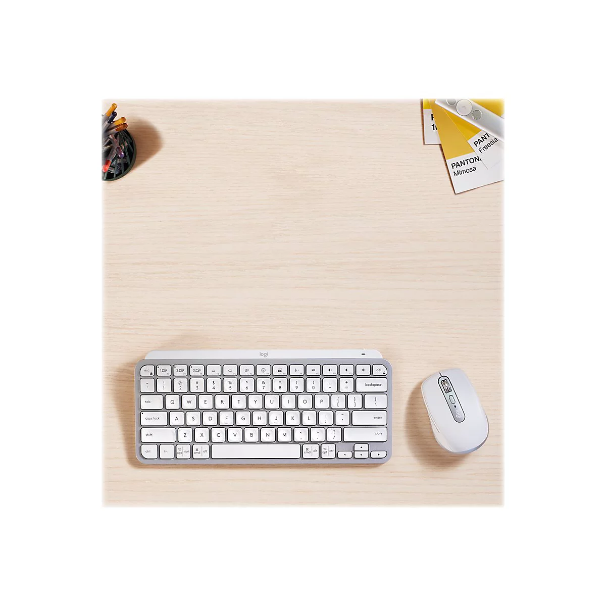 Draufsicht auf ein hellgraues Logitech-Keyboard und eine Maus auf einer Holzoberfläche, daneben Stifte und Farbfächer.