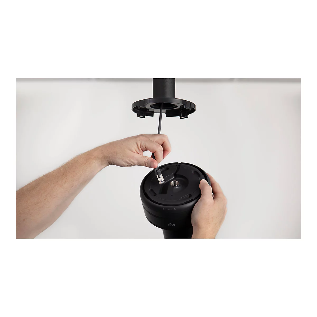 Une personne connecte un câble réseau à un produit noir Logitech. La personne tient le câble à deux mains tout en le branchant.