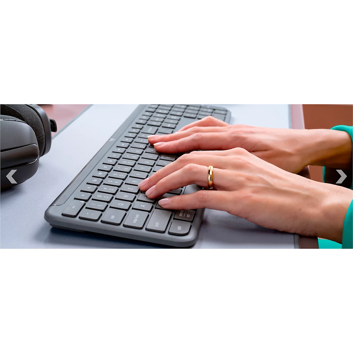 Hands typing on keyboard, ring on finger. Headphones in the background.