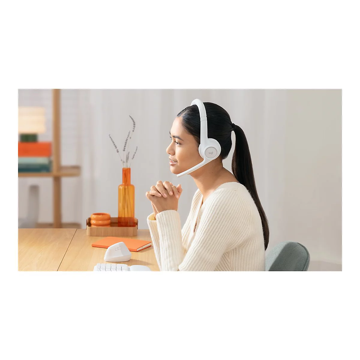 Junge Frau mit Headset. Sie sitzt am Tisch, verschrÃ¤nkt die HÃ¤nde und blickt nachdenklich zur Seite.