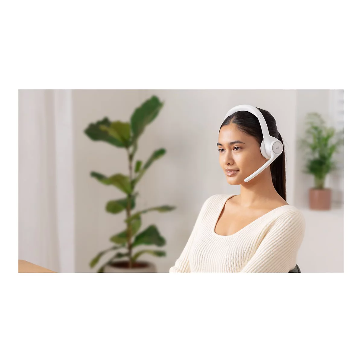 Junge Frau mit Headset im BÃ¼ro. Sie blickt leicht zur Seite, im Hintergrund Pflanzen.