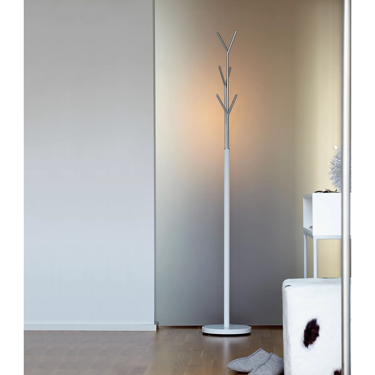 White design coat rack in a modern setting. To the right a stool, to the left a wall. Grey slippers are on the floor.