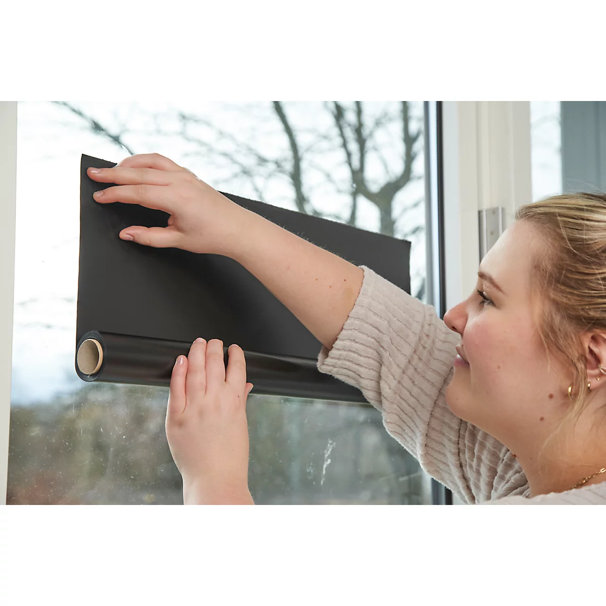 Eine Frau befestigt eine schwarze Fensterfolie an einem Fenster. Sie wirkt konzentriert.