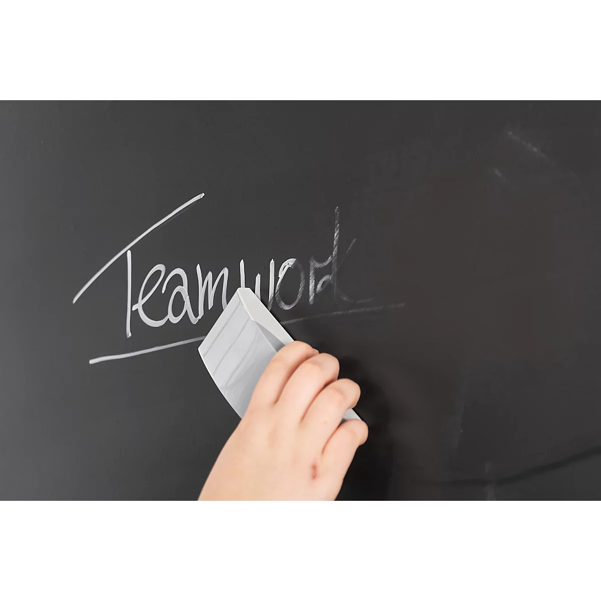 Hand wischt mit Schwamm 'Teamwork' von Tafel. Kreide Schriftzug fast entfernt.