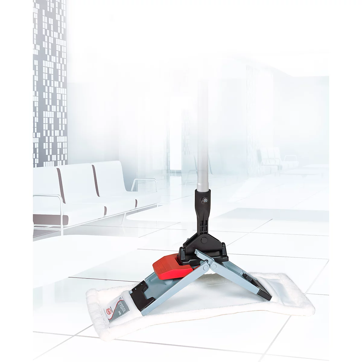 Grey mop with red lever stands on a light tiled floor. In the background, a bright waiting area with white furniture.