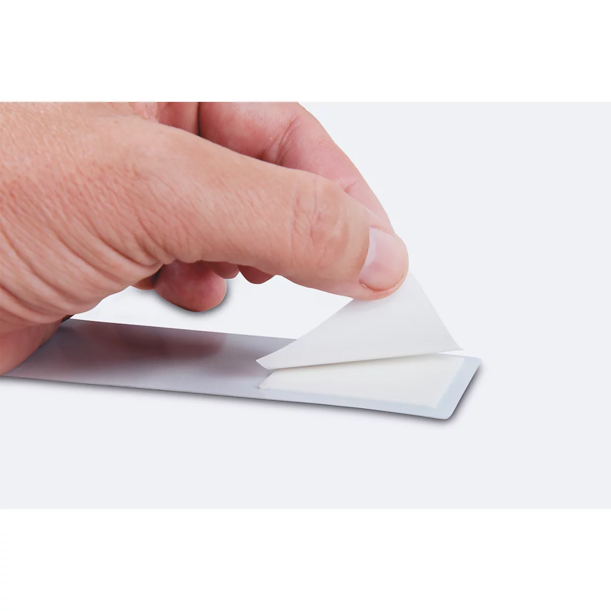A hand peels a white sticker from a grey strip.