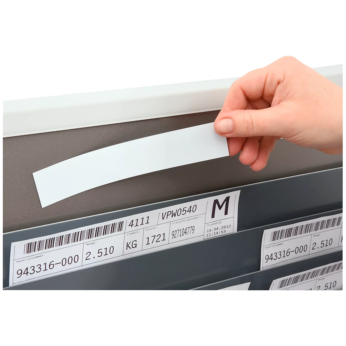 Hand holding a white sticker over labels in a shelf.