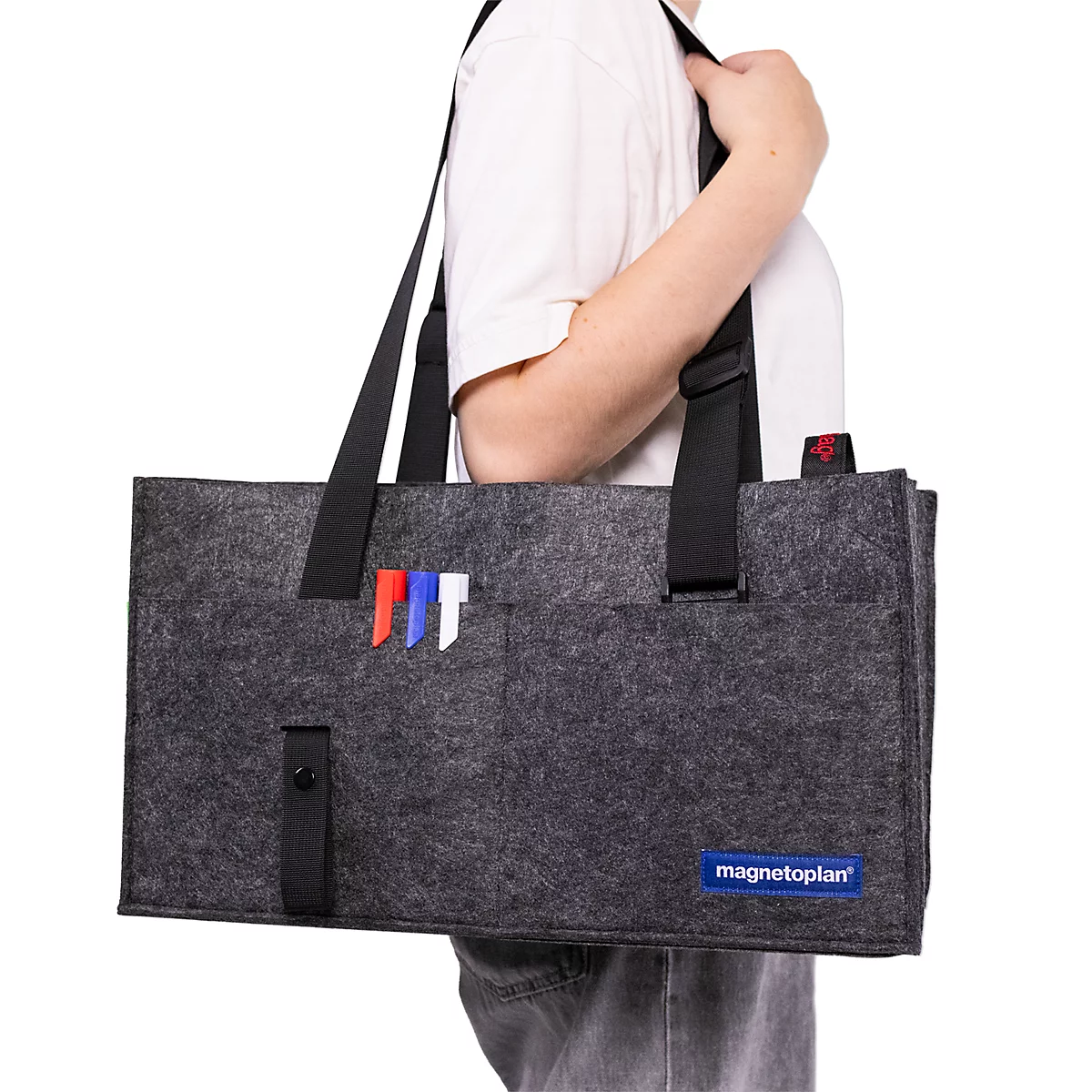 Een persoon draagt een grijze vilten tas met pennenhouder en Magnetoplan-logo over de schouder.