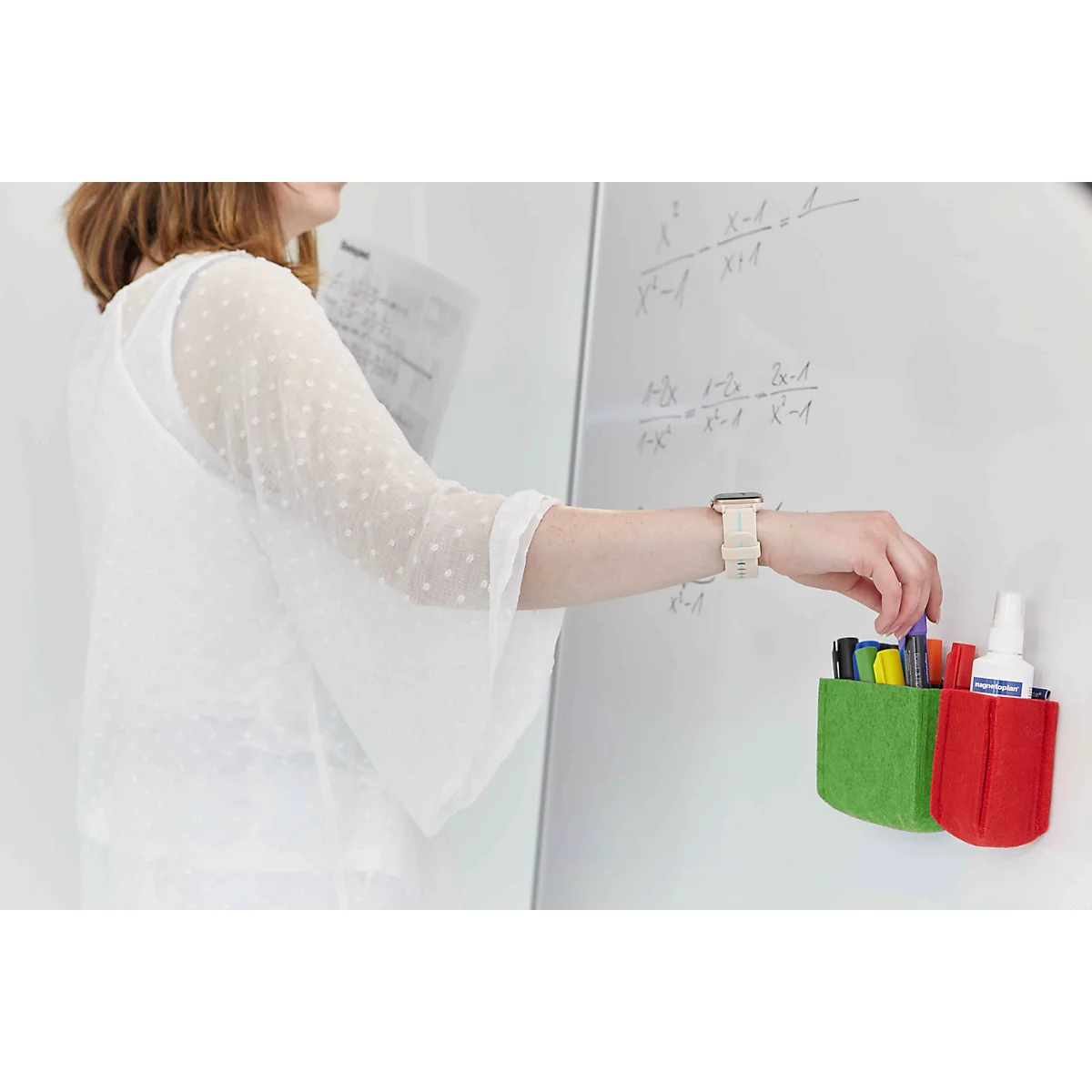 Eine Frau greift an einer Whiteboard-Tafel nach einem Stift aus grünen und roten Filz-Stiftehaltern.