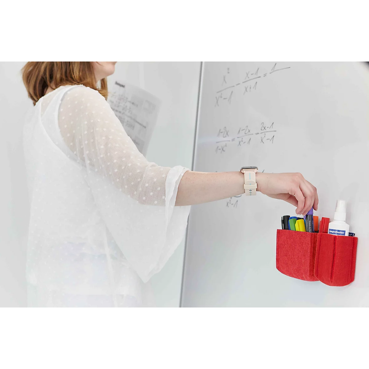 Eine Lehrerin nimmt einen Stift aus einem roten Filz-Organizer, der an einem Whiteboard befestigt ist.