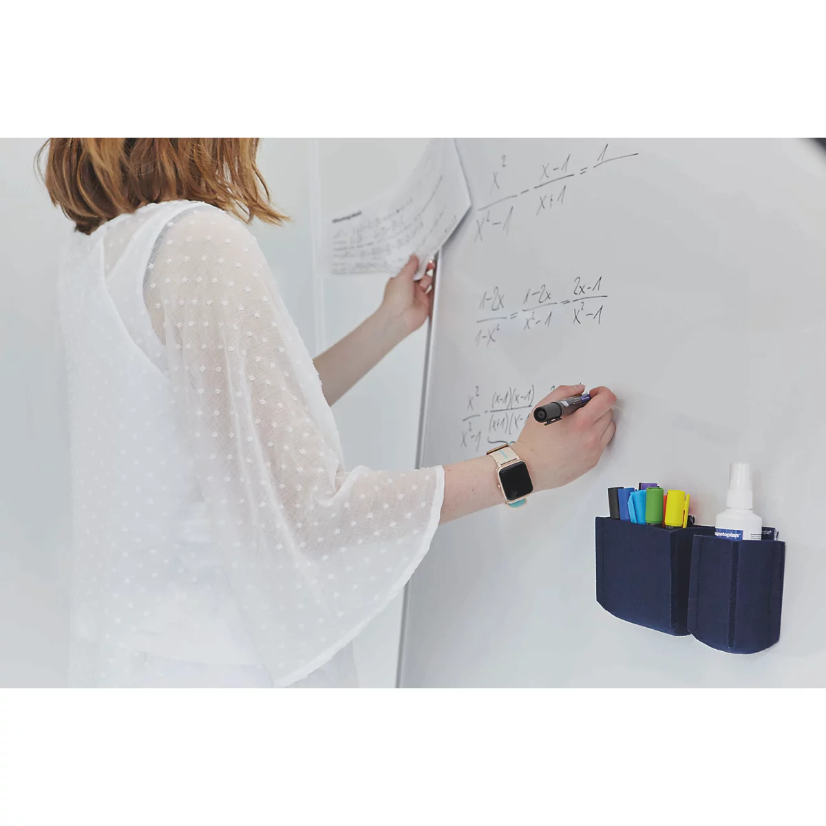 Een vrouw in een witte blouse schrijft wiskundige formules op een whiteboard met een marker.