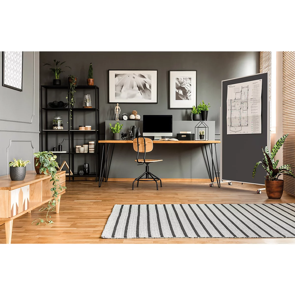 Modernes Heimbüro mit Schreibtisch, Computer, Regal und Pflanzen vor einer dunklen Wand.
