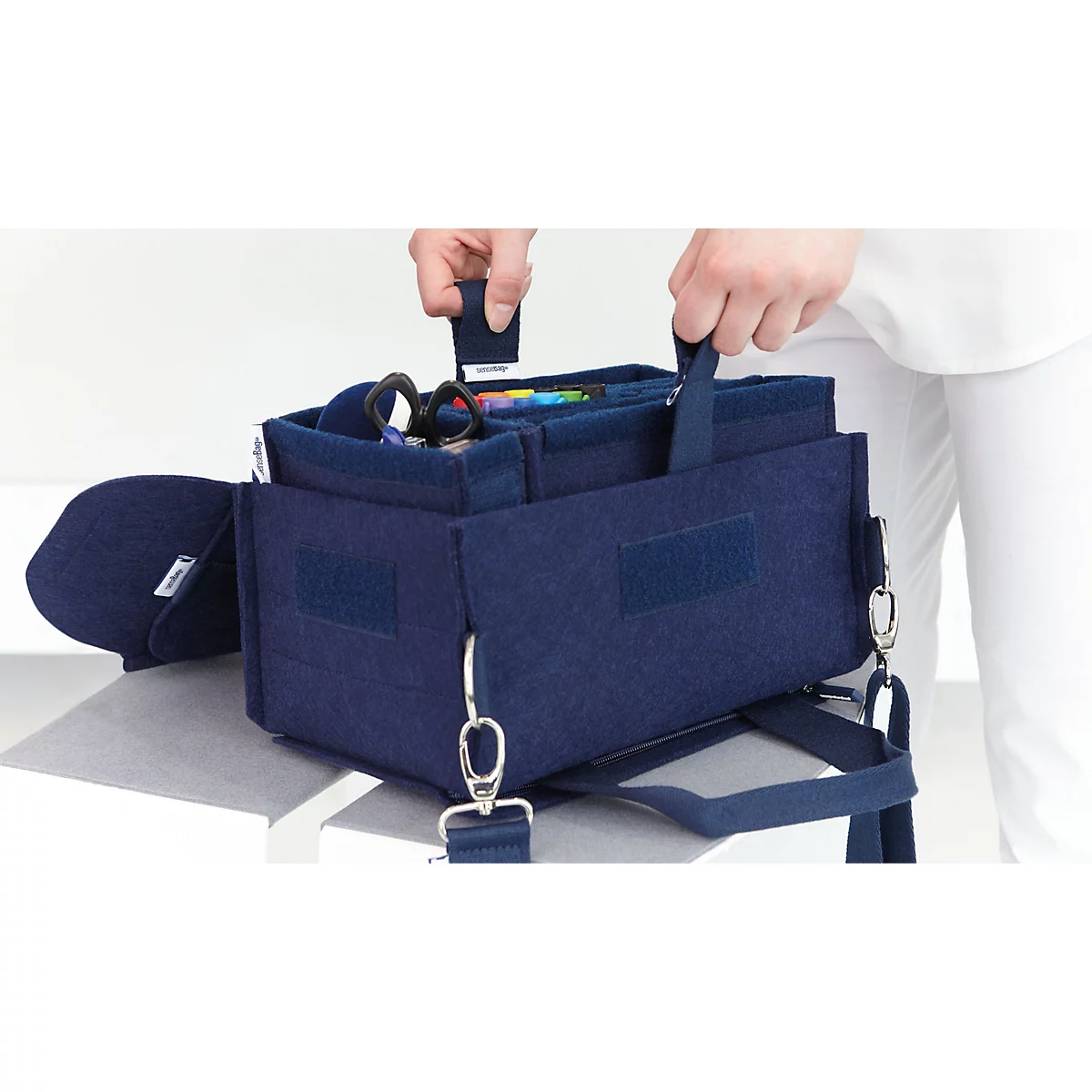 Hände heben eine dunkelblaue Filzbox mittels praktischem Liftgurt aus einer Halterung.