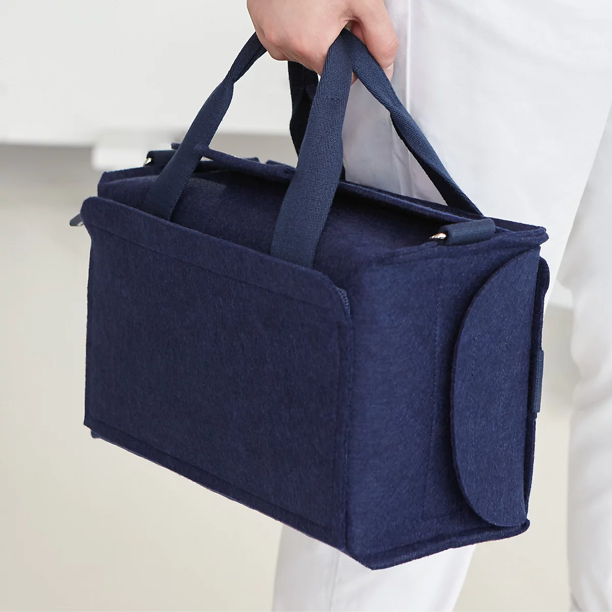 Eine dunkelblaue Filztasche wird per Schlaufe flexibel am Griff eines schwarzen Rollkoffers befestigt.