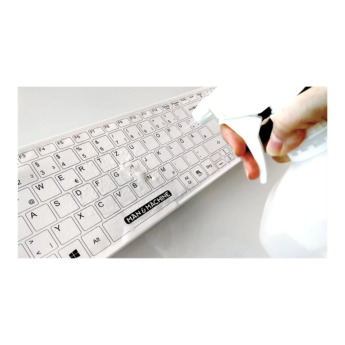 Weiße Tastatur mit Aufschrift MAN & MACHINE, wird mit einer Sprühflasche desinfiziert.
