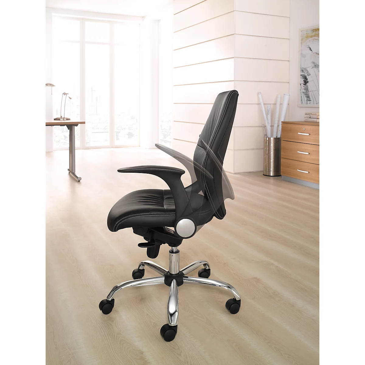 Black office chair with adjustable armrests and backrest. On light-colored floor in front of window and furniture.