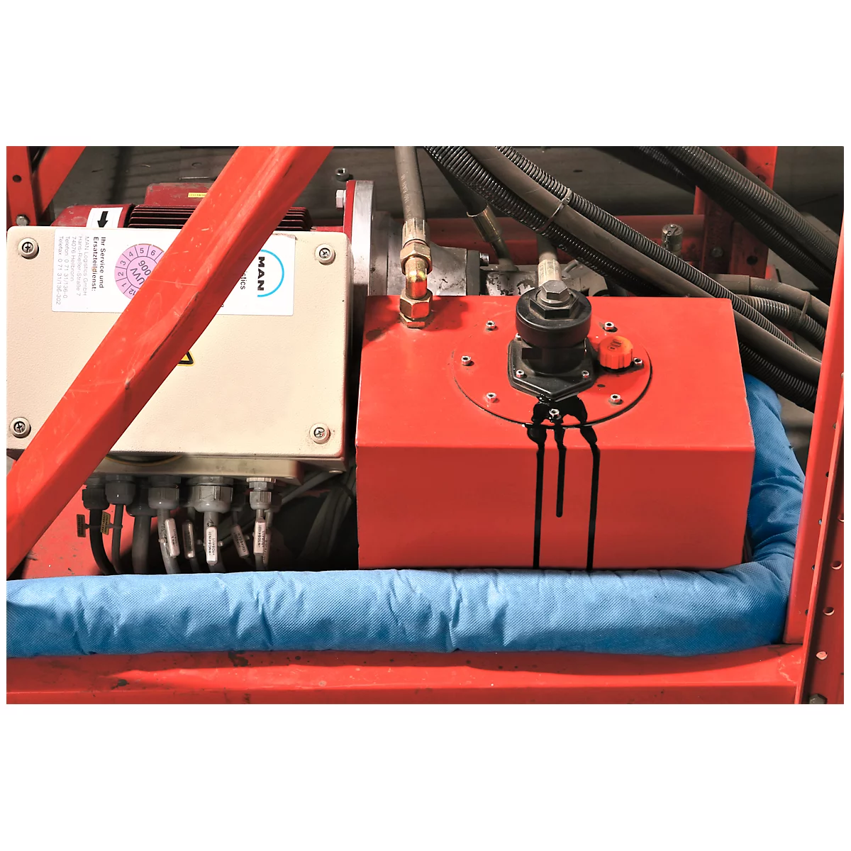 Piezas de máquina: contenedor rojo con aceite derramado, junto a una caja gris. Cojín azul debajo del contenedor, marcos rojos.