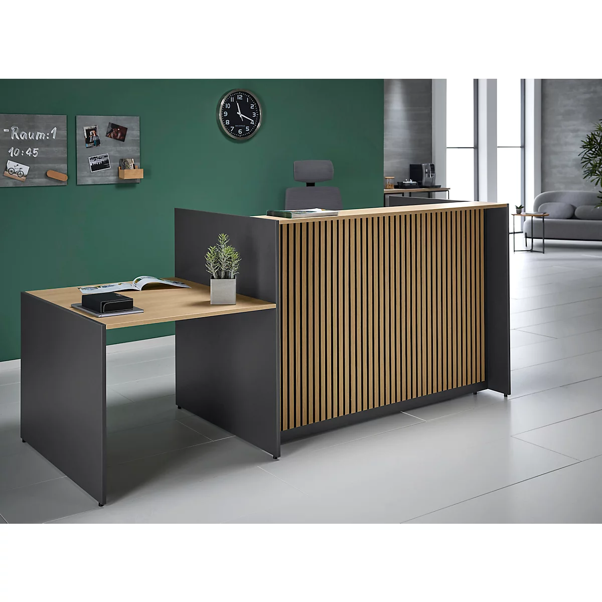 Receptiebalie met houten lamellen, groene muur erachter, klok, aantekeningen. Bureau, plant, open boek.