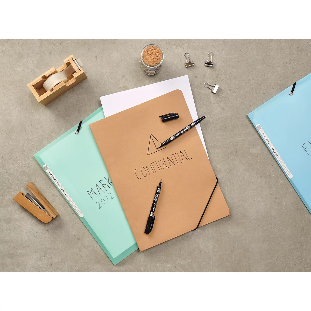 Plusieurs chemises à documents, stylos et fournitures de bureau sur une surface grise.