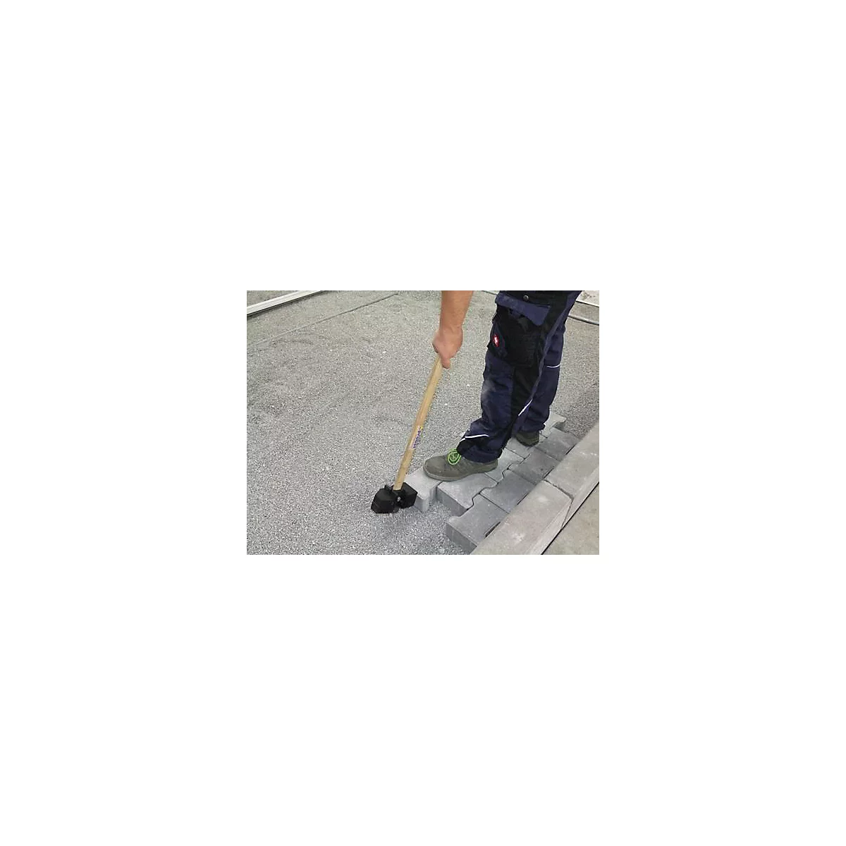 Un ouvrier pose des pavés avec un marteau. Il se tient sur les pierres, tient le marteau et les frappe.