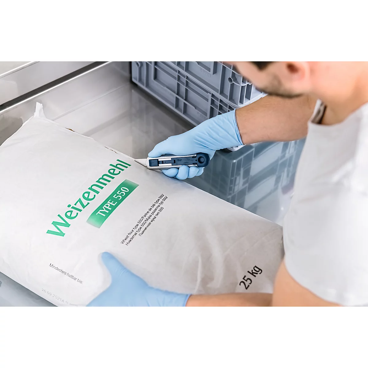 Person mit blauen Handschuhen schneidet einen Mehlsack mit der Aufschrift "Weizenmehl Type 550" auf.