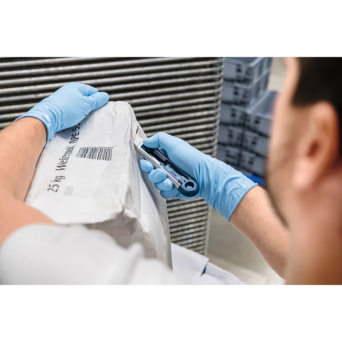 Person in blauen Handschuhen schneidet mit einem Messer einen Sack mit Weizenmehl auf. Barcode und Schriftzug sind sichtbar.