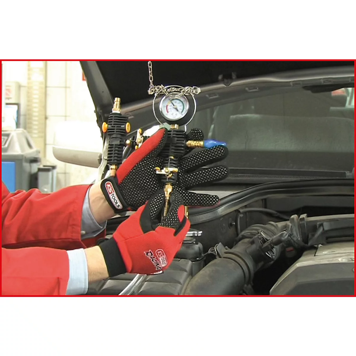 Mechaniker in roter Jacke und Handschuhen misst den Druck in einem Motorraum mit einem Messgerät.