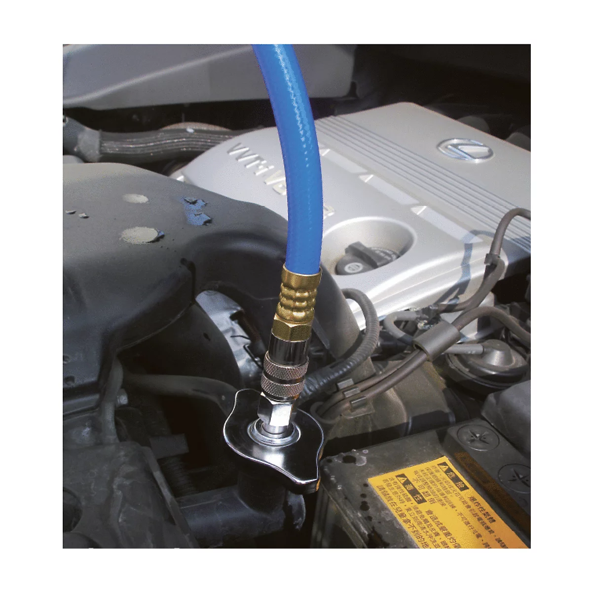 Blauer Schlauch an einem Kühlmittelbehälter im Motorraum eines Autos. Der Deckel wird geöffnet.