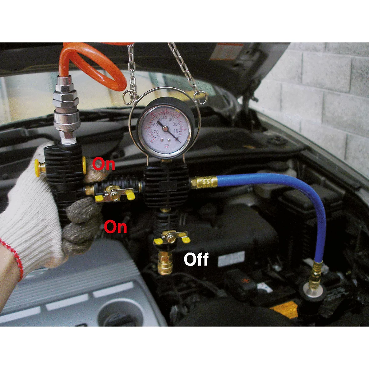 Ein Mann in einem Handschuh hält ein Werkzeug, das mit einem Auto verbunden ist. Auf dem Werkzeug steht "On" und "Off", außerdem ist ein Messgerät zu sehen.