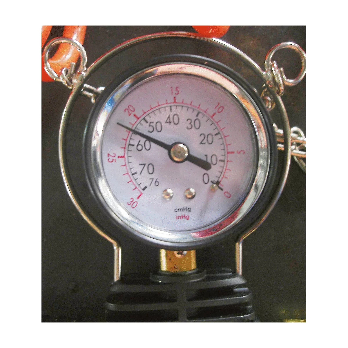Ein rundes Manometer mit schwarzem Rahmen, weißem Zifferblatt und roter Nadel. Der Zeiger zeigt ca. 10 an.