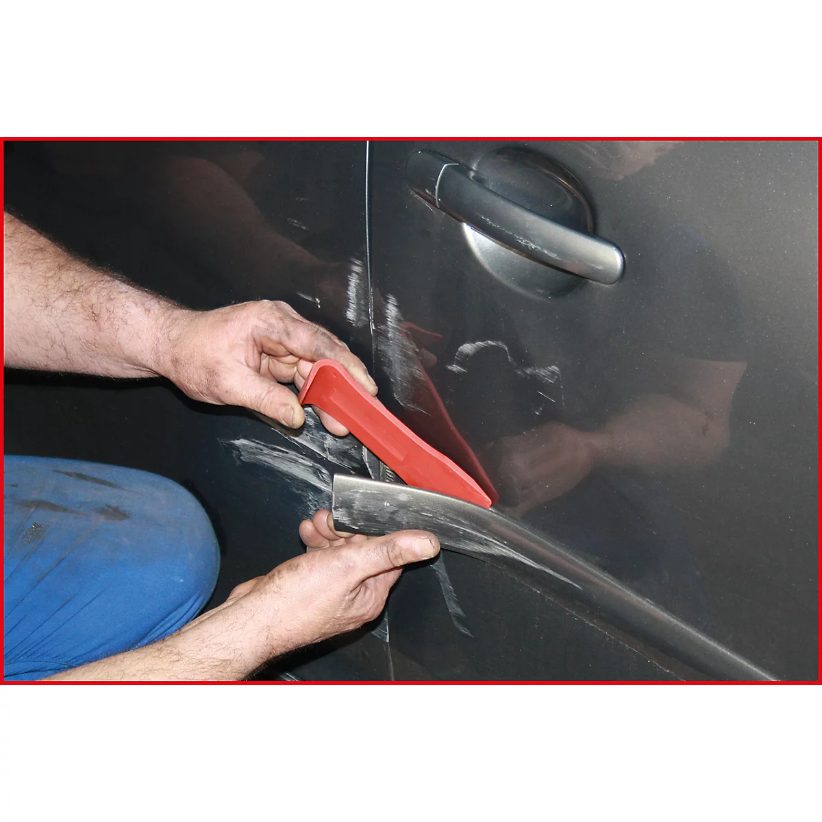 Hände eines Mechanikers, der eine Stoßstange an einem Autotür montiert. Mit rotem Werkzeug werden Leisten eingesetzt.