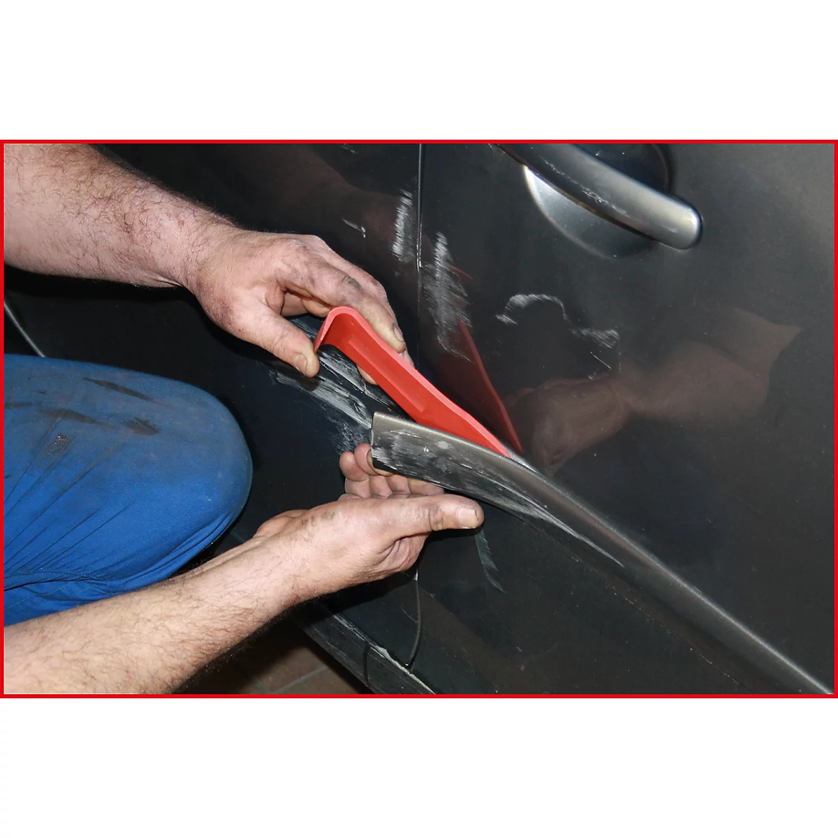 Nahaufnahme von Händen, die mit einem roten Werkzeug einen schwarzen Streifen an einer Autotür befestigen.