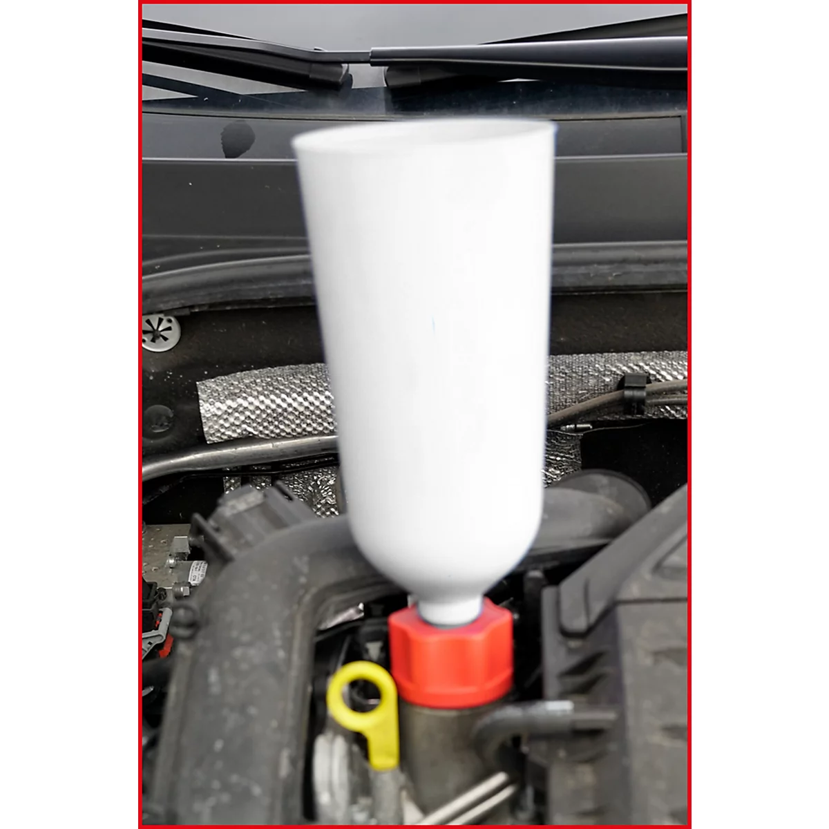 Weißer Trichter im Motorraum eines Autos. Der Trichter ist in eine Öffnung mit rotem Deckel gesteckt.