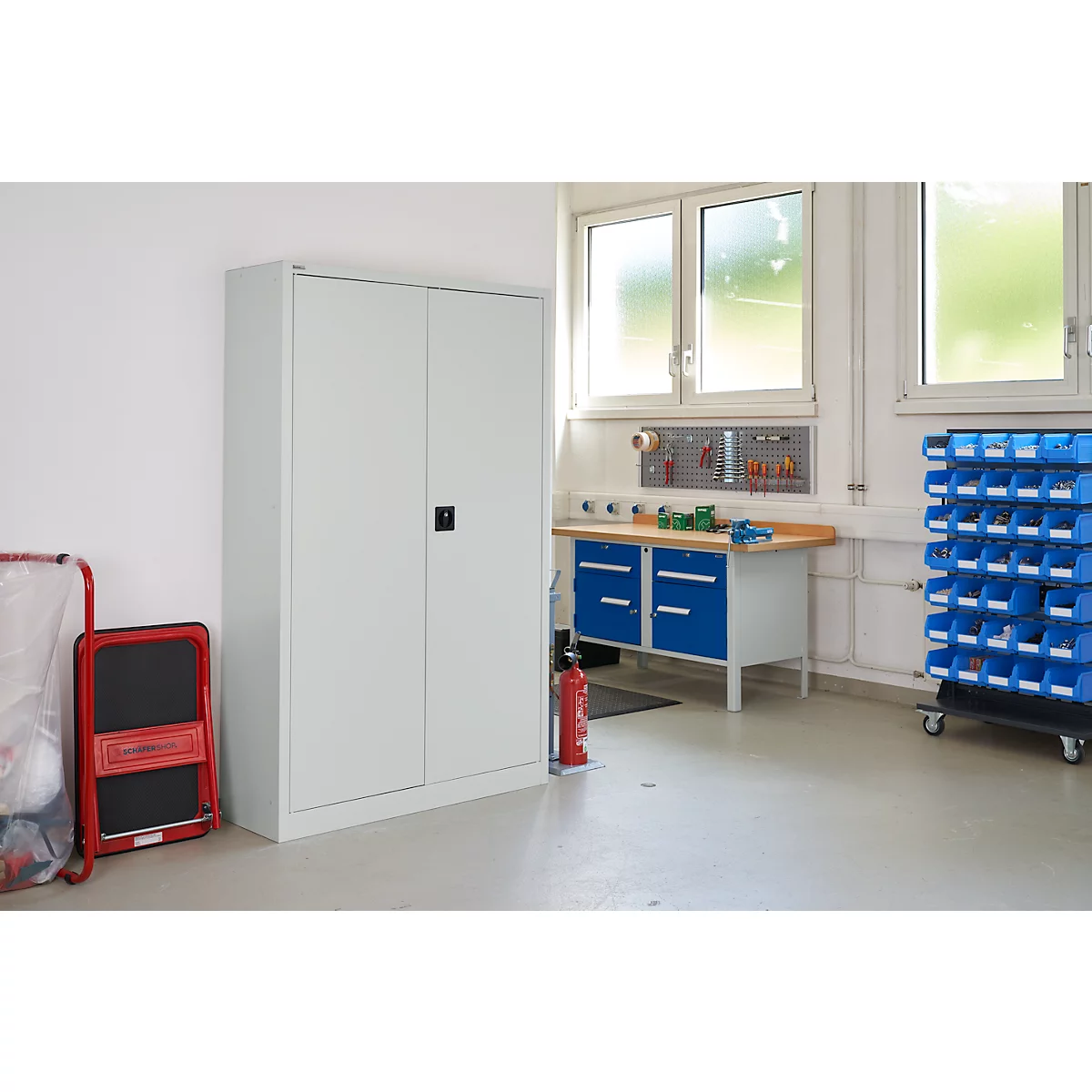 Werkplaats met grote grijze kast, blauwe werkbank, sorteerbakken en rode brandblusser.