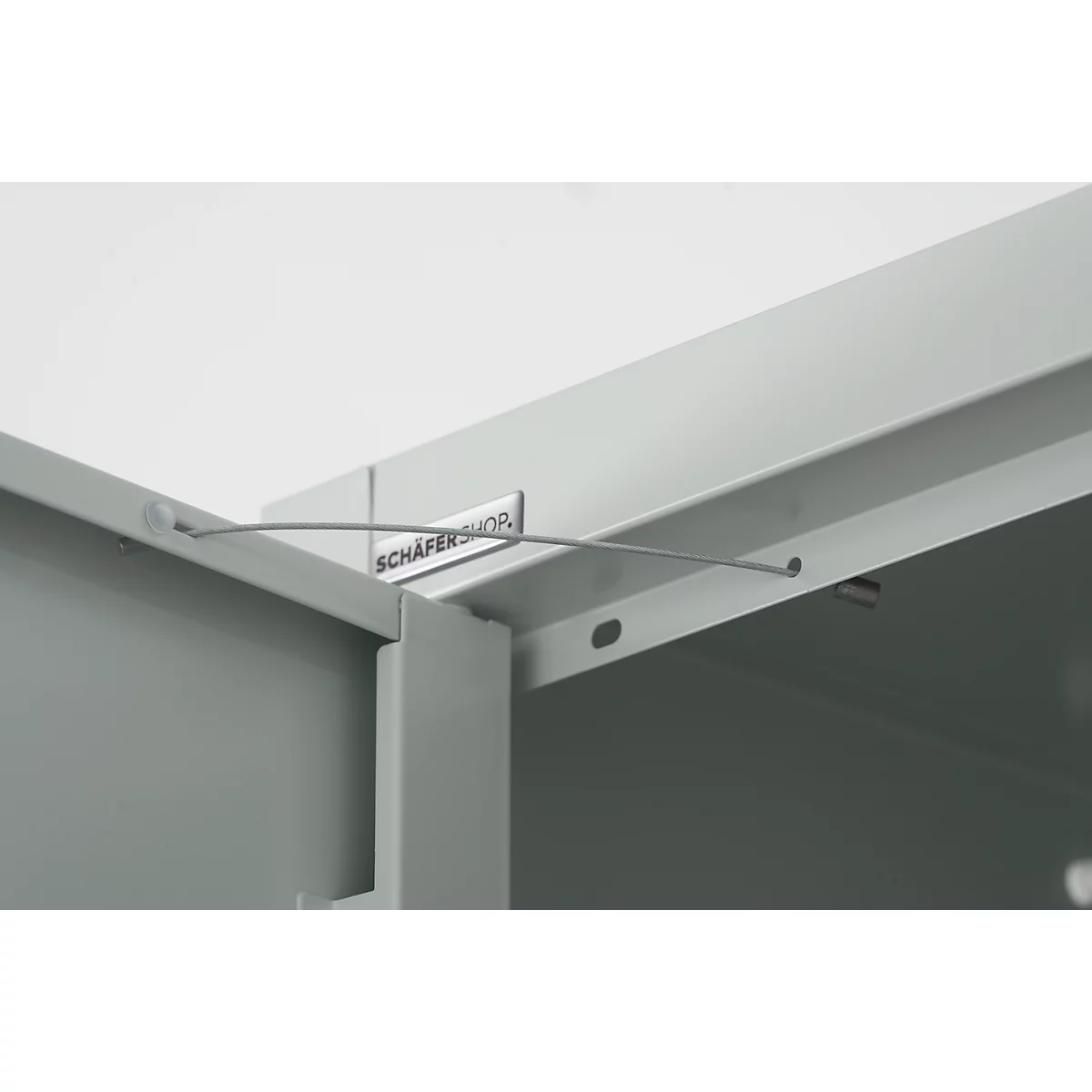 Detailopname van een metalen kast met de tekst 'SCHÄFERSHOP'. Een dunne draad spant zich tussen twee bevestigingen.