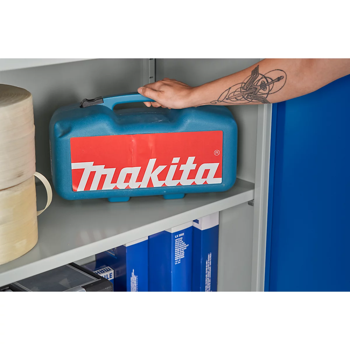 Persoon die een blauwe gereedschapskist met rood Makita-logo in een plank vasthoudt.