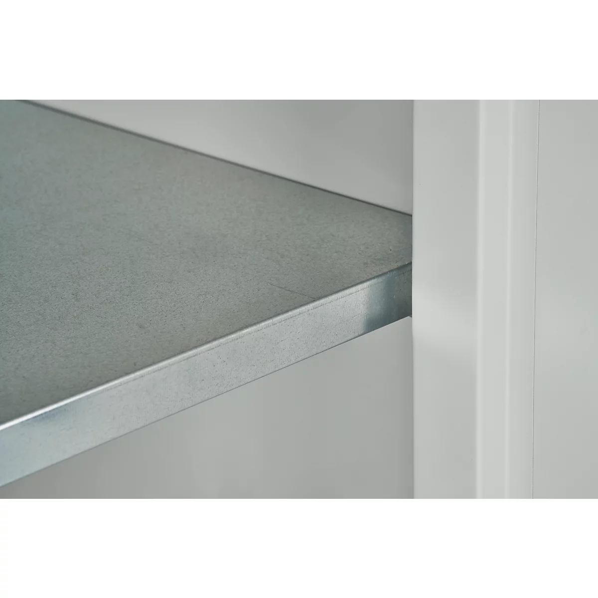 Close-up van een metalen plank, grijs, met witte muur ernaast.