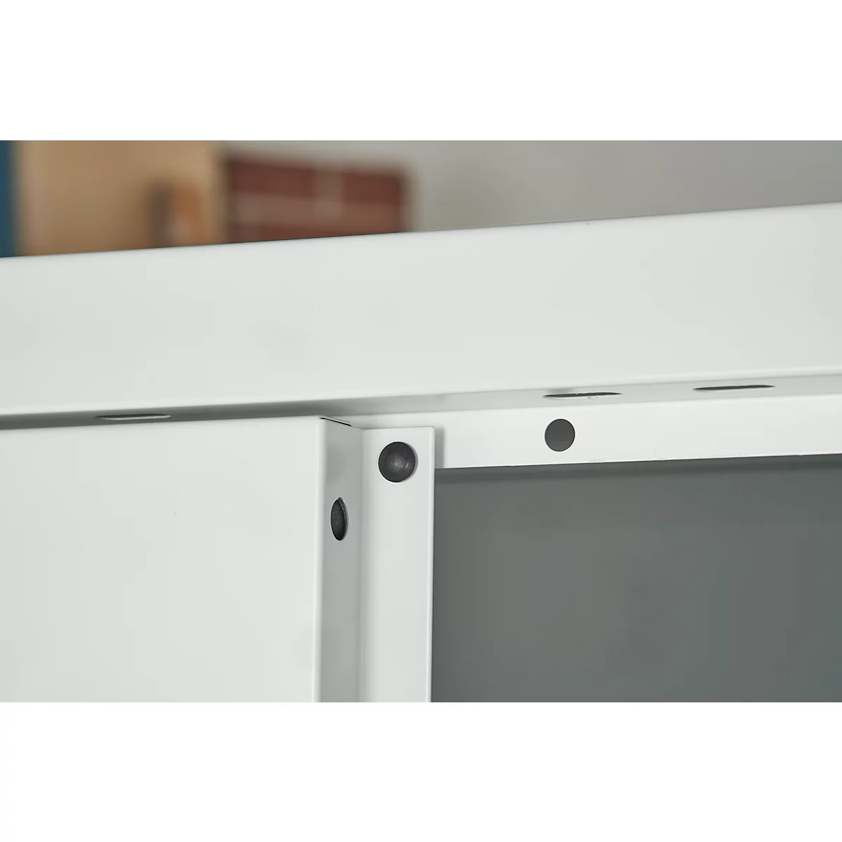 Close-up van een wit meubelframe met zwarte schroeven en gaten.