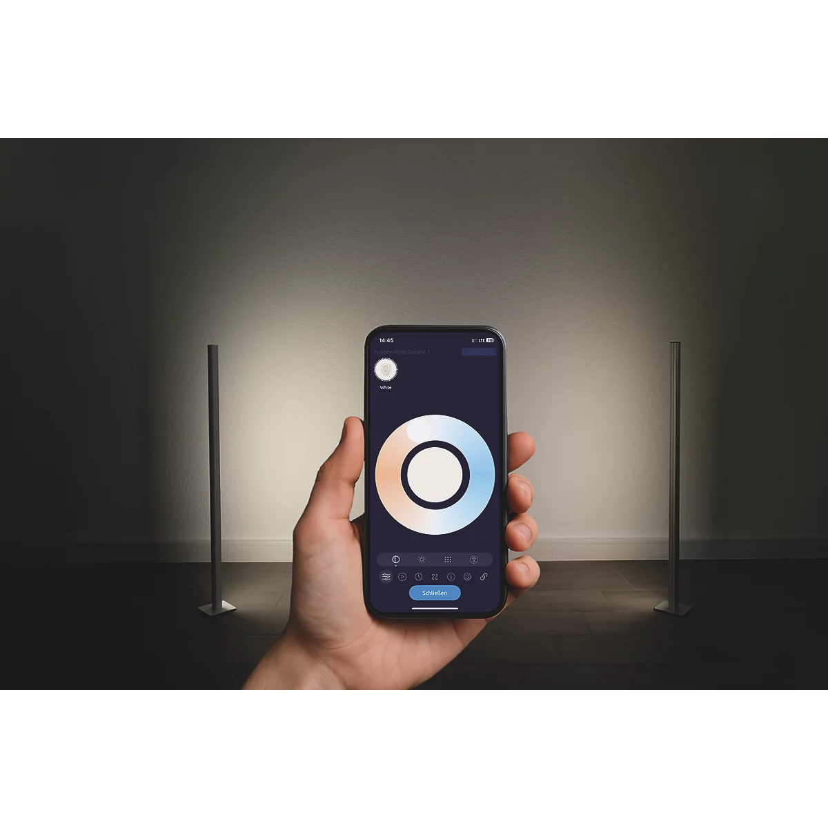 Eine Hand hält Smartphone mit Farbsteuerung. Zwei schlanke Lampen stehen im Raum.
