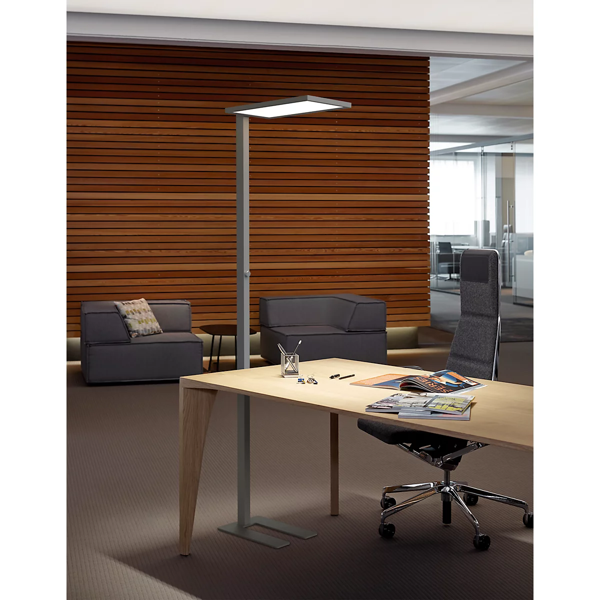 Moderne Stehleuchte neben einem hellen Holztisch in einem stilvollen Büro mit Holzlamellenwand.