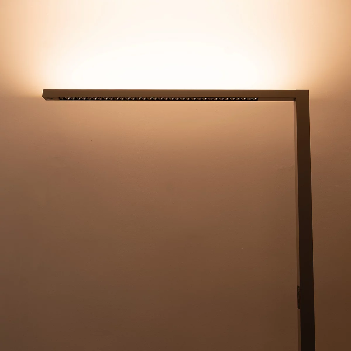 Eine minimalistische, dunkle LED-Stehleuchte wirft warmes, indirektes Licht an die Wand.