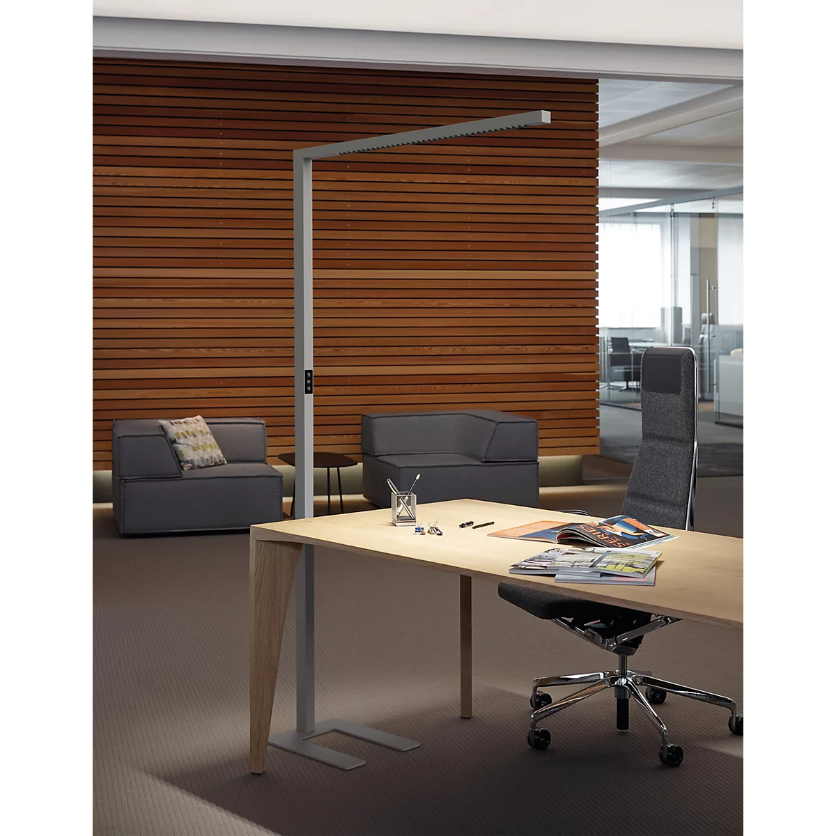 Moderne Stehleuchte beleuchtet einen hölzernen Schreibtisch in einem eleganten Büro mit Holzlamellenwand.