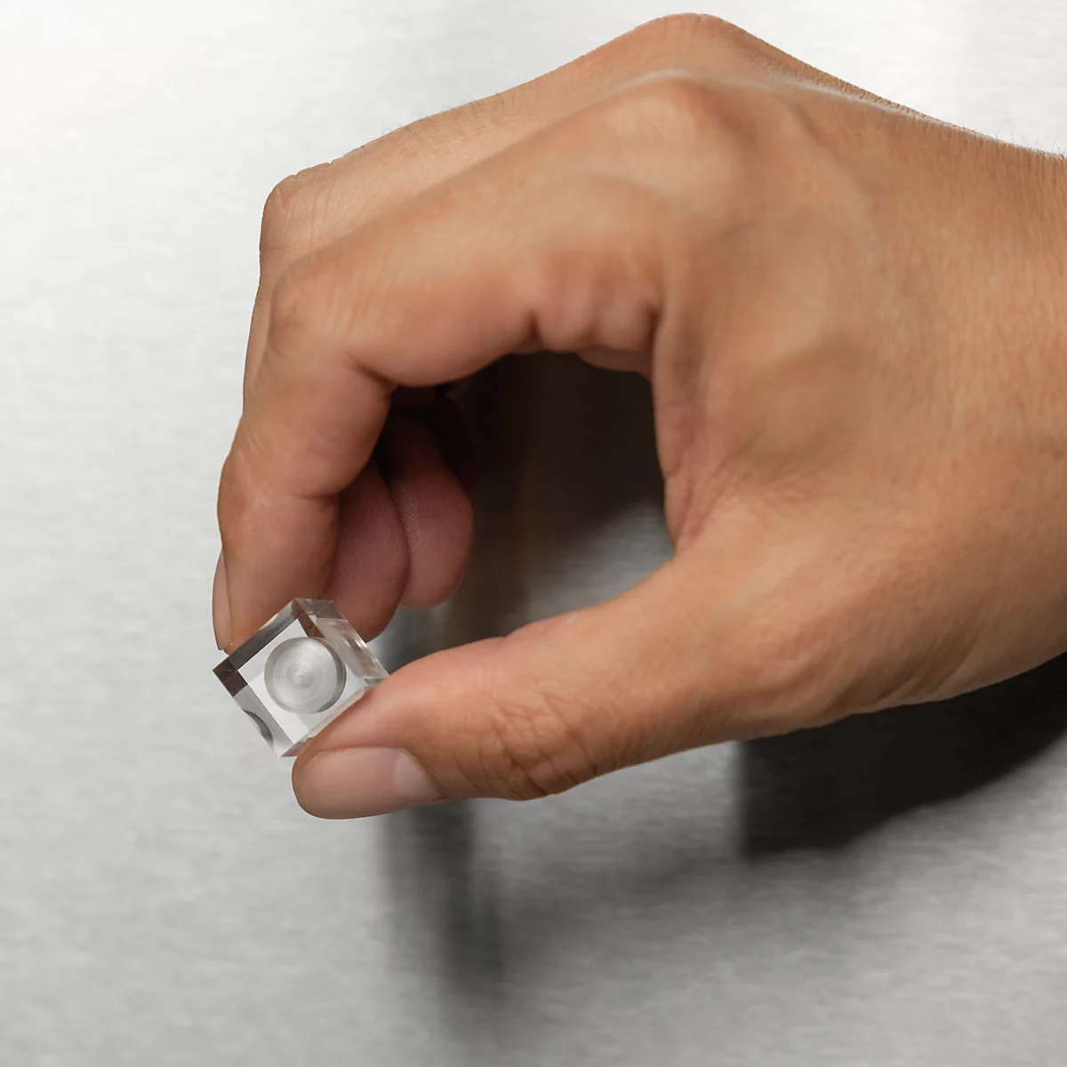 Hand hält einen kleinen, durchsichtigen Würfel mit einem zentralen runden Element.