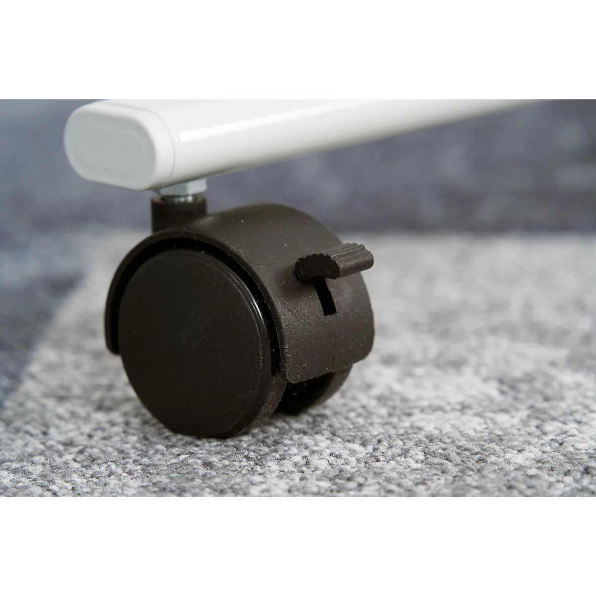 Close-up of a black furniture wheel with locking lever. Above, a white furniture leg.