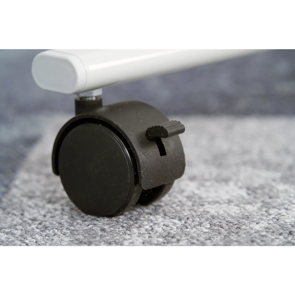 Close-up of a black caster with a brake, connected to a white, cylindrical element.