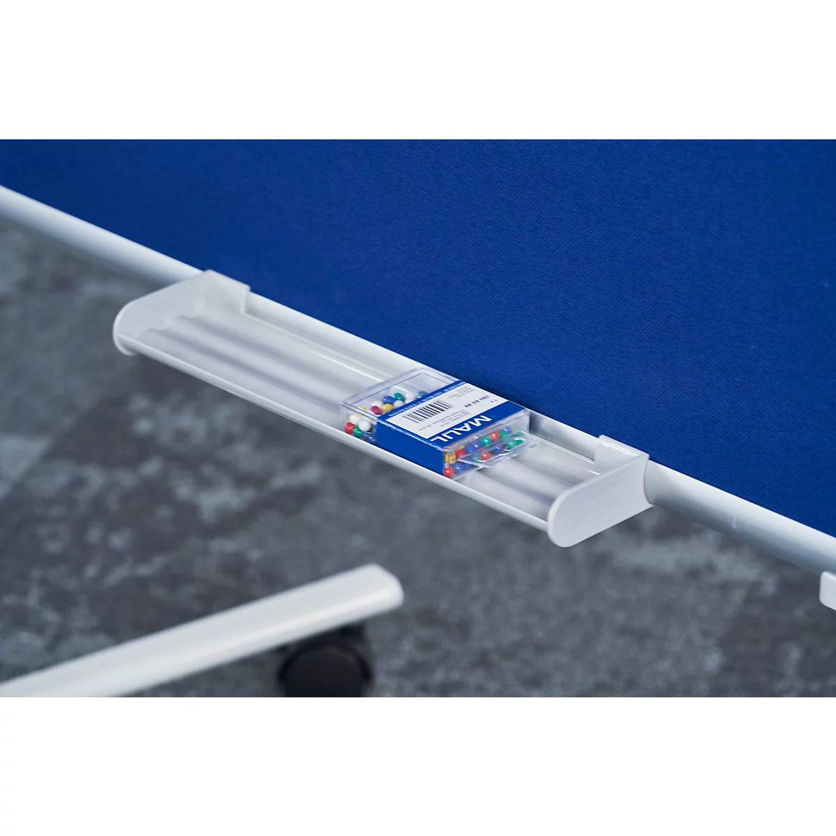 A white holder with push pins on a blue pinboard. A pen is located in the lower area of the picture.