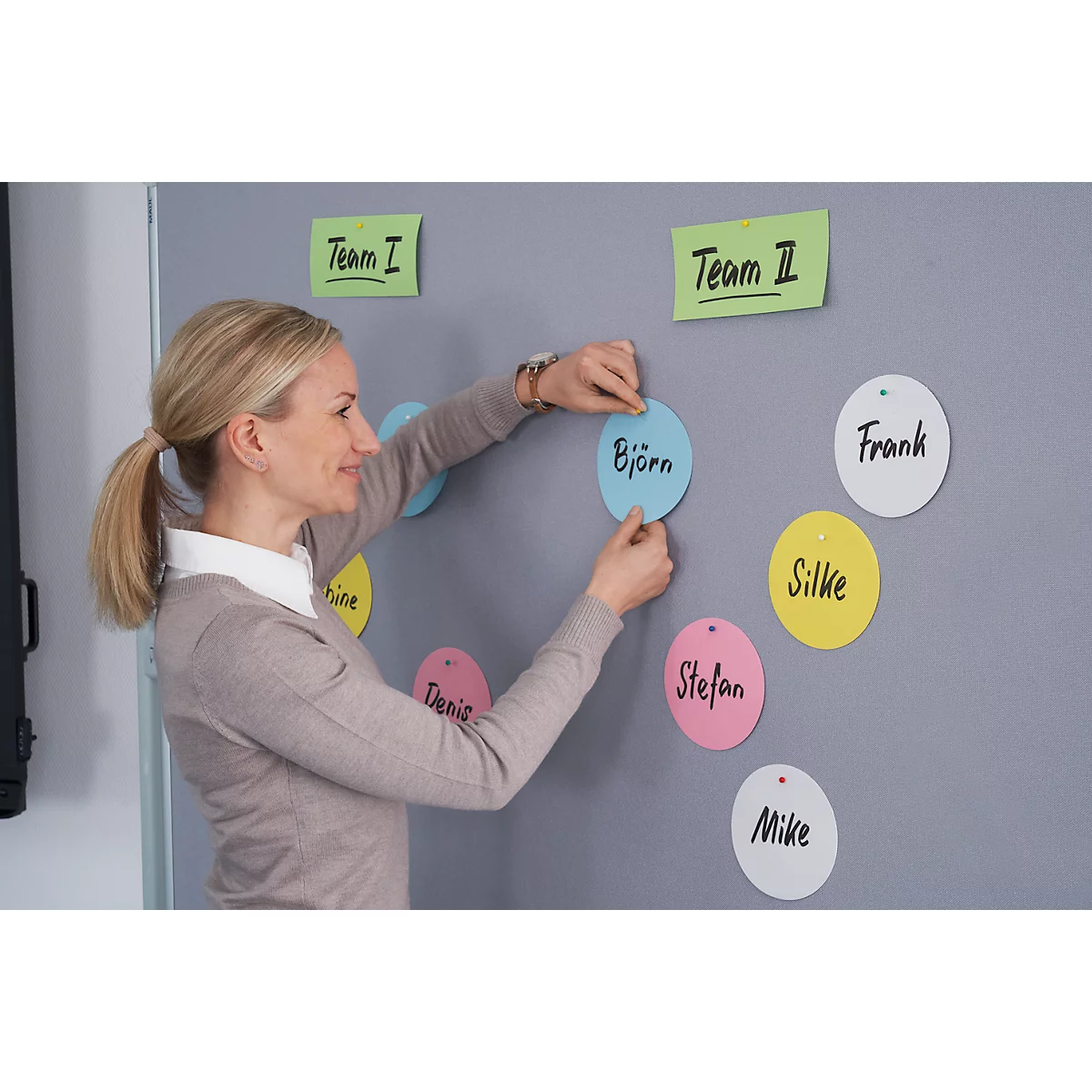 A woman is arranging name tags on a wall. The wall has the inscriptions 'Team I' and 'Team II'.