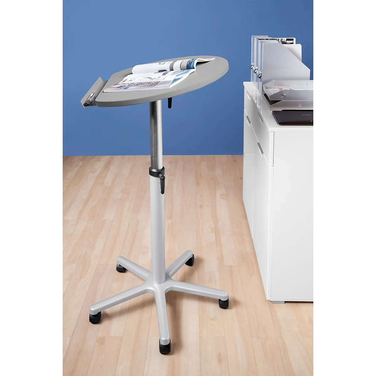 Grey standing table with magazines, in front of blue wall and white cabinet. On light wooden floor.