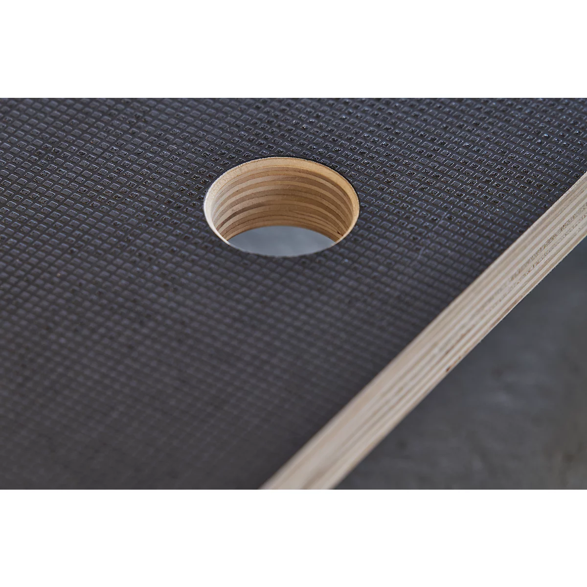 Close-up of a circular hole in a dark, textured material, next to an edge of light wood.