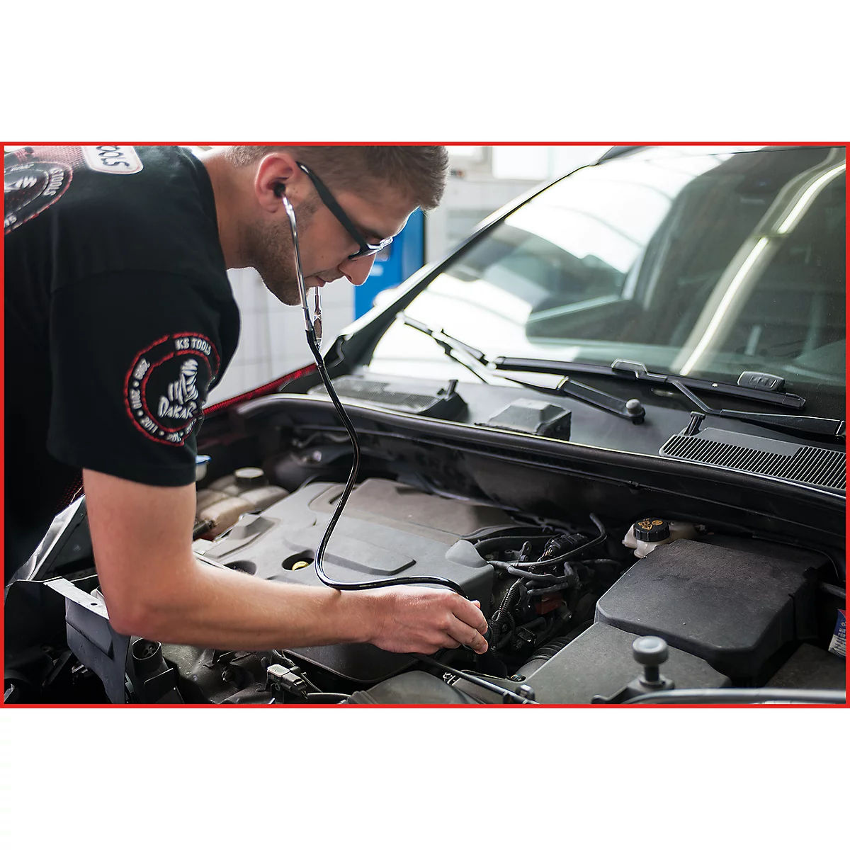 Ein Mechaniker hört mit einem Stethoskop den Motor eines Autos ab.